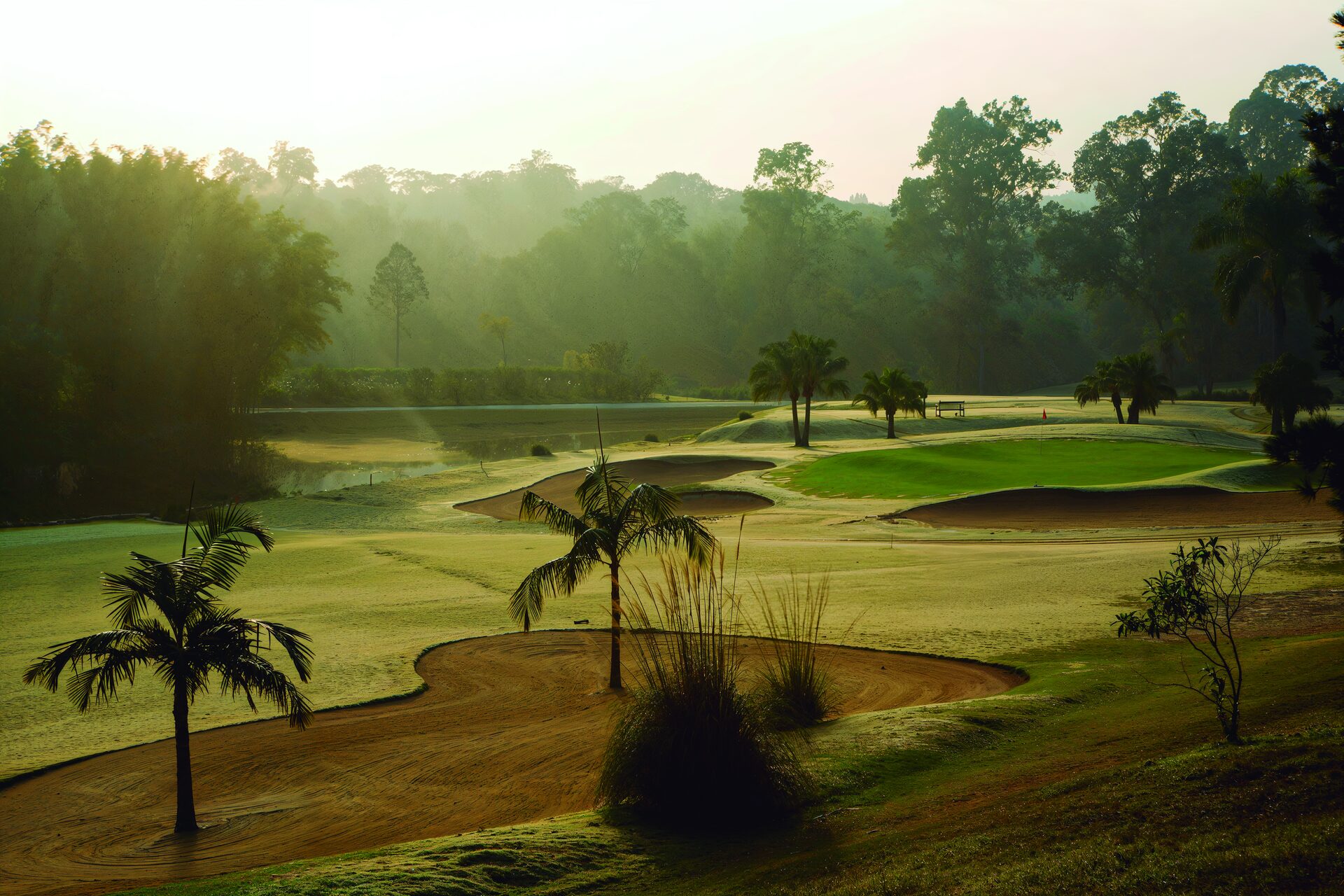 Vista aérea do campo de golfe ao entardecer, com fairways, bunkers e a sede do clube ao fundo